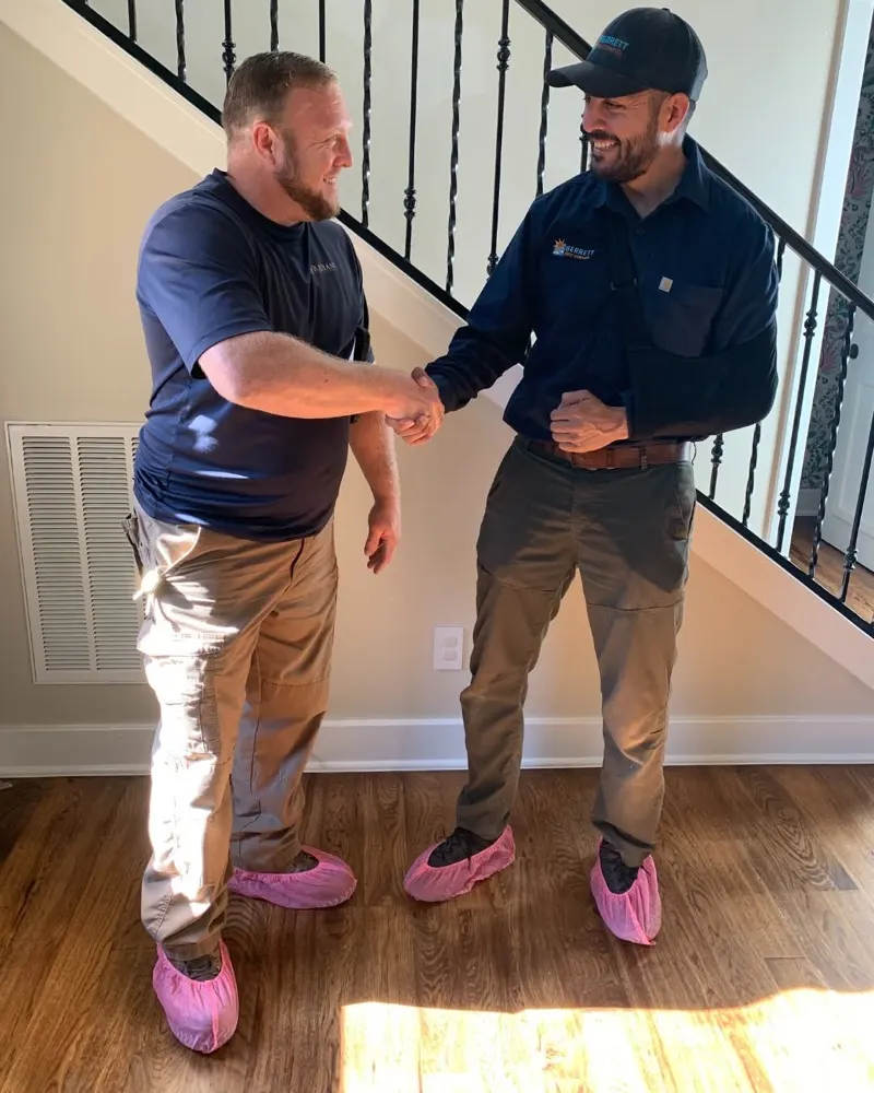 Radiant technician shaking hands with a partner, both wearing pink shoe covers