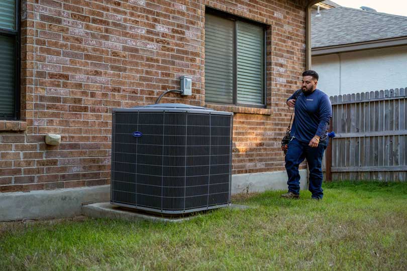 A Radiant HVAC technician walks up to the AC condenser in a home's backyard.