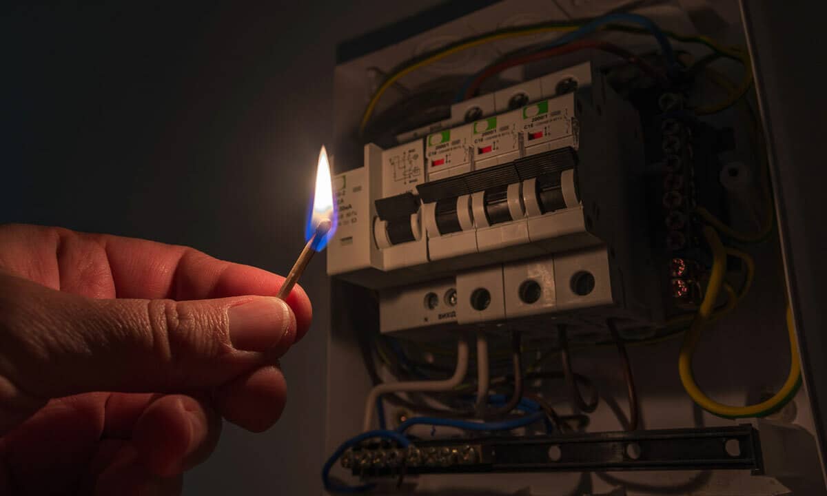 A person with a lit match trying to look at their circuit breakers in the electrical panel.