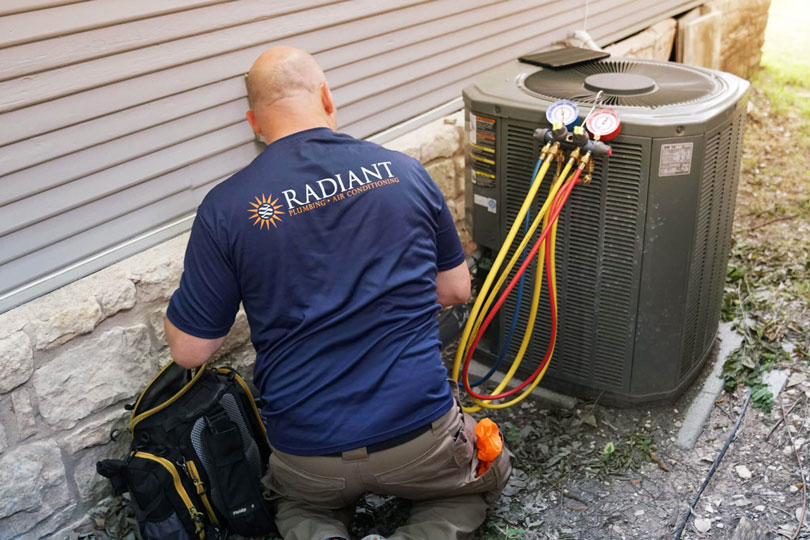 A Radiant HVAC technician testing and repairing an outdoor AC unit