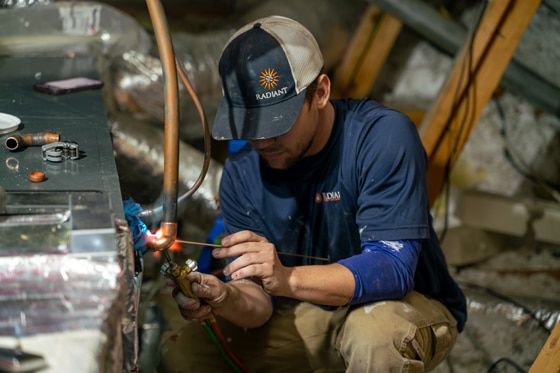 Radiant HVAC technician repairing a furnace in an Austin attic