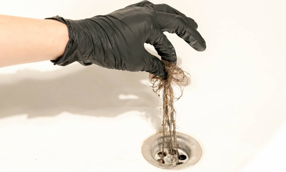 Someone pulling a hair clog from a shower drain