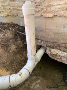 The vertical cleanout pipe attached to the main horizontal drain, up close where the house pipes connect