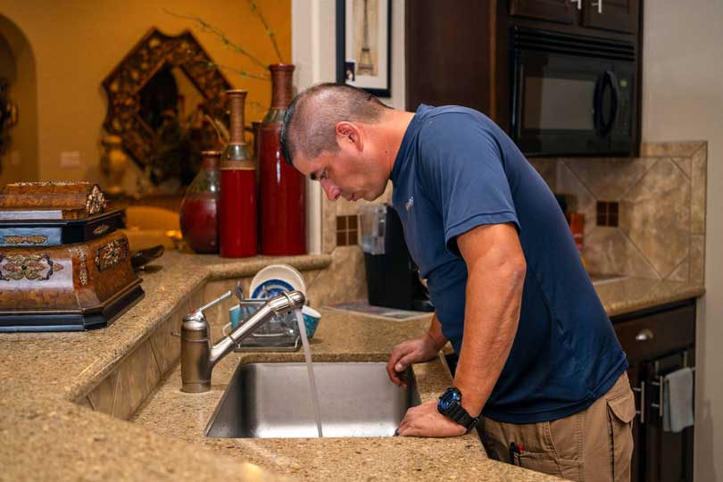 A Radiant plumber inspecting a kitchen sink faucet and drain