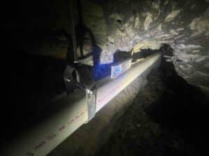new PVC sewer line secured under home with pipe hangers during drain replacement