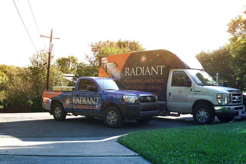 Two Radiant Plumbing & Air Conditioning trucks parked on a street next to each other.